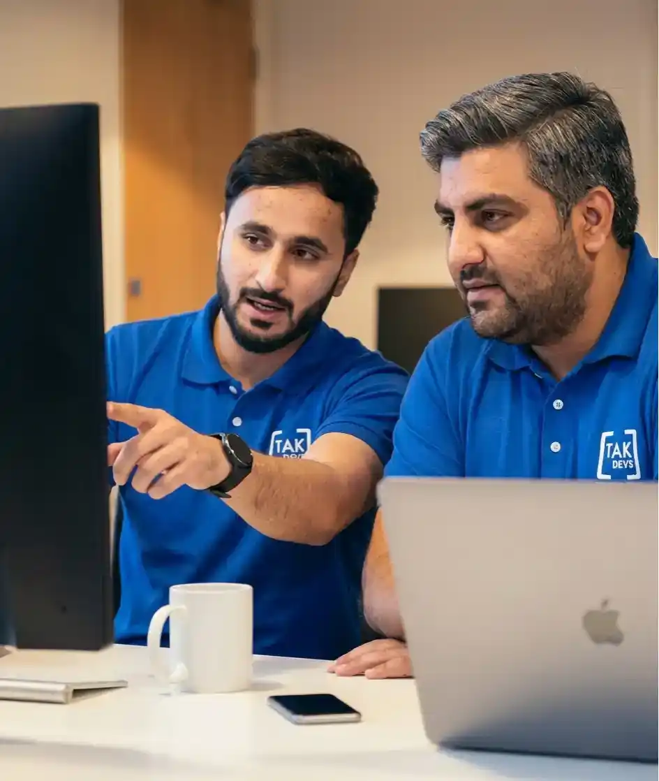 Two software developers collaborating over a laptop, discussing coding and project solutions in an office setting.